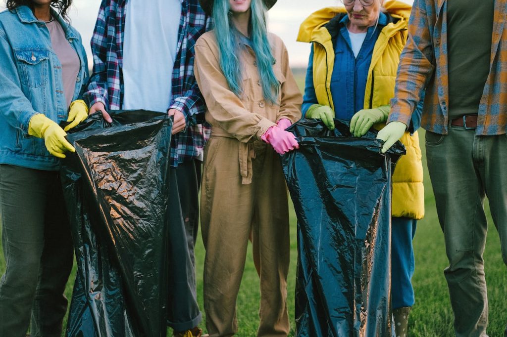 Diverse volunteers cleaning up a field, holding large trash bags and wearing gloves.