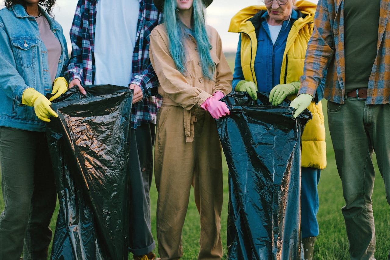 Diverse volunteers cleaning up a field, holding large trash bags and wearing gloves.